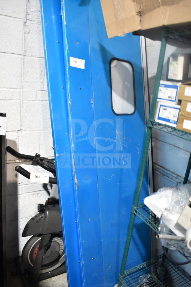 Two blue kitchen traffic doors with small windows, showing surface wear and marks. Tags display number 152, indicating auction lot.