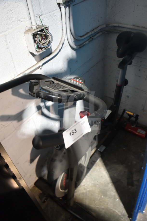 D615 Stationary Exercise Bicycle with adjustable seat and handlebars. Auction tag 153 visible. Good condition.