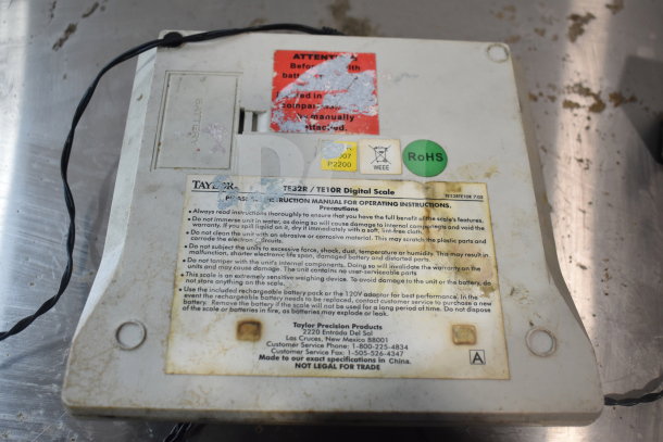 Taylor TE32R Countertop Scale, visible instructions, some wear and stickers, including RoHS and caution labels.