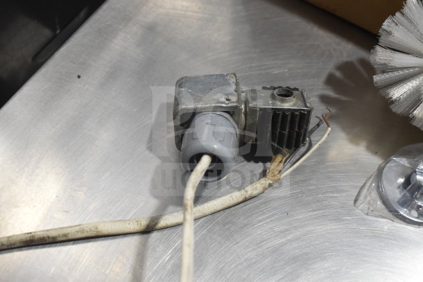 10 assorted items including a brush and metal component with wire, part number 600IB1918S, on a metallic surface.