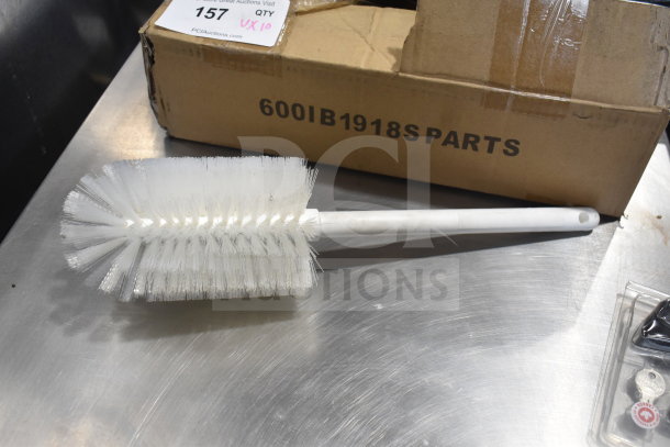 White brush with long handle, labeled "600IB1918S PARTS," on metal surface near box with auction tag. Good condition.