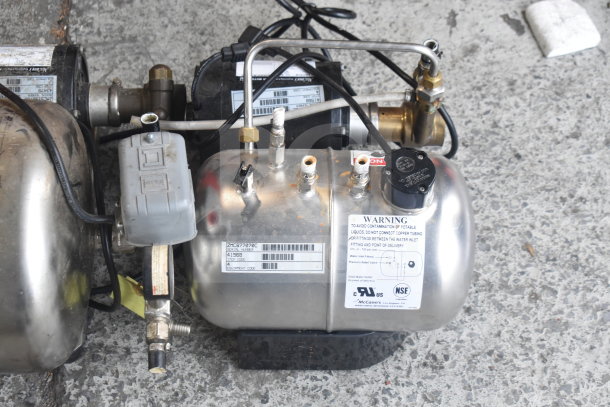 Two McCann's carbonators, stainless steel, used condition. Features warning labels, pressure relief valve, various connectors.
