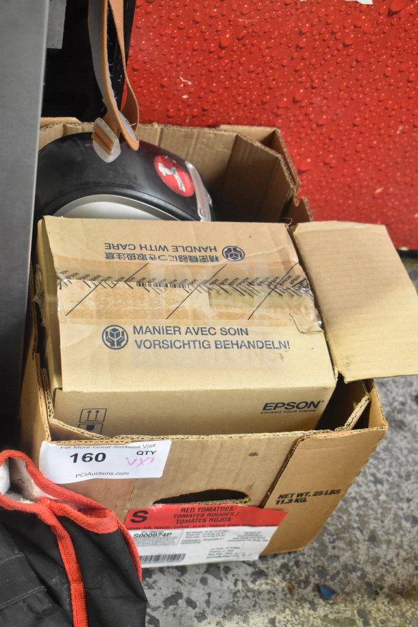 Box containing Dymo label printer and Epson receipt printers, models M129H and M244A, with packaging showing "Handle with Care."