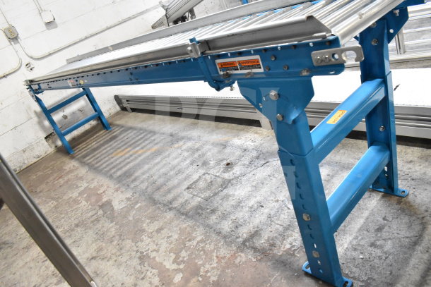 Hytrol floor style roller conveyor, blue frame, metal rollers, used condition, visible warning labels, industrial equipment.