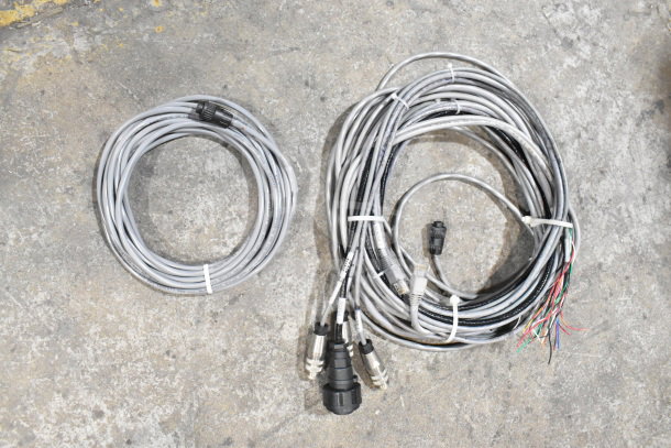 Two coils of gray cables, one with exposed wires and connectors, on a concrete surface; part of a mixed auction lot.