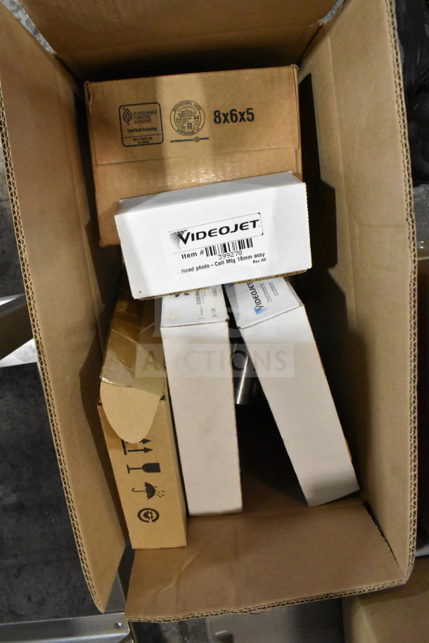 Box containing various VideoJet items including head photo and label sensor, packaged and ready for auction.