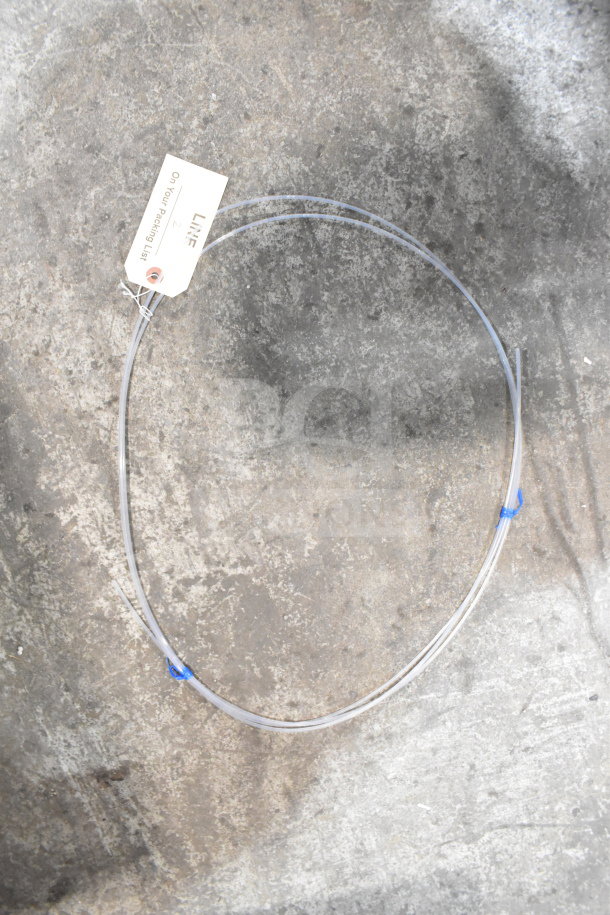 Coiled clear cable with a tag marked "Line 25, On Your Packing List," against a concrete backdrop.