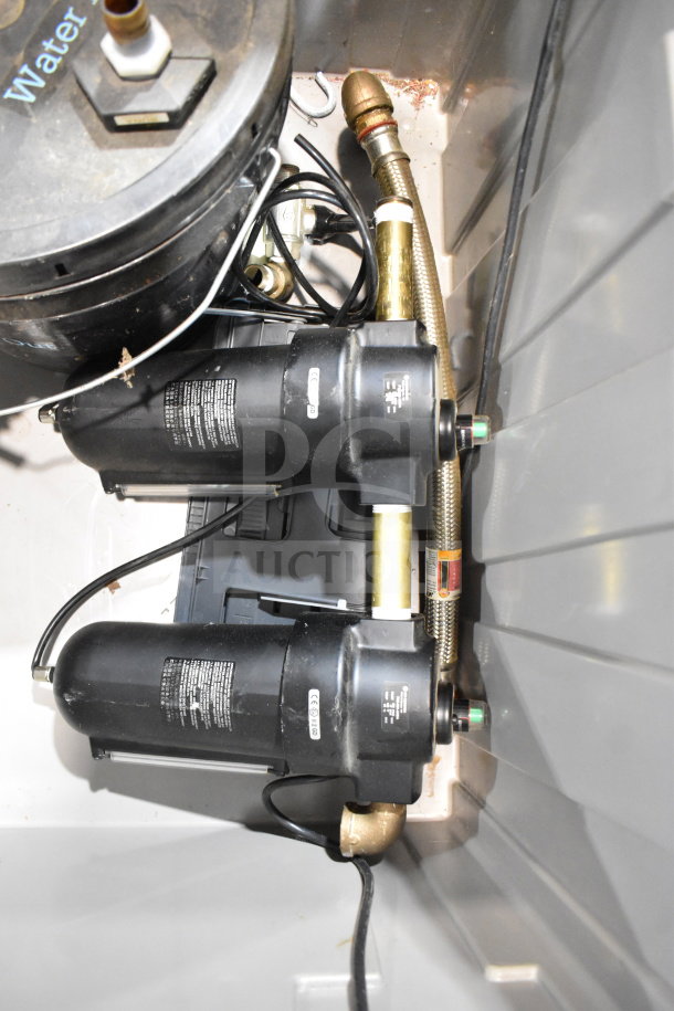 Bin containing black water filter system with attached hoses and wiring, moderate wear, visible label text and CE markings.