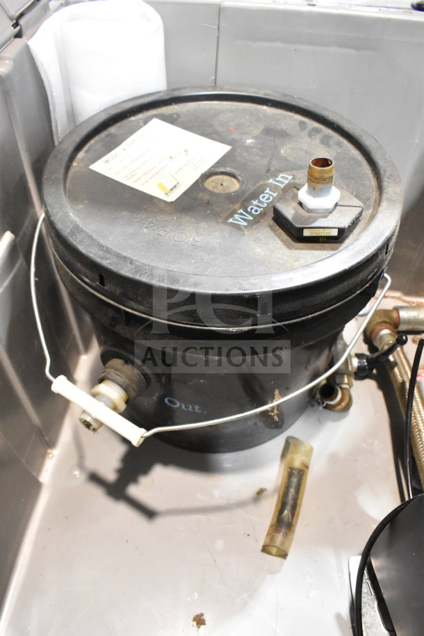 Bin containing a used water filter and buckets, featuring labeled inlets and outlets. Includes manufacturer tag on lid.