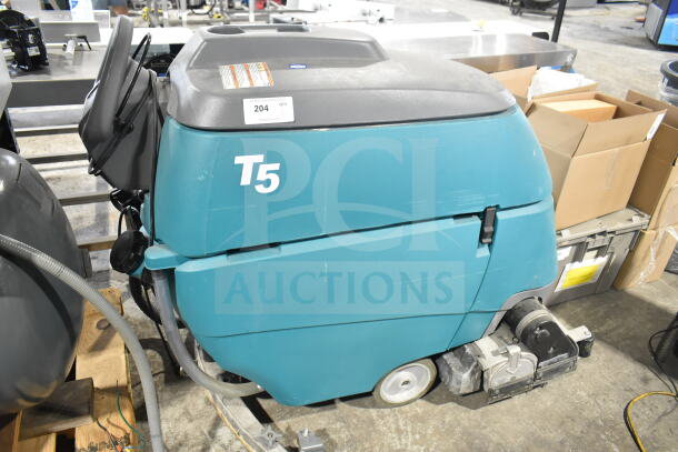 Tennant T5 floor cleaning machine in teal, shown in used condition. Visible label with model name and auction lot sticker.