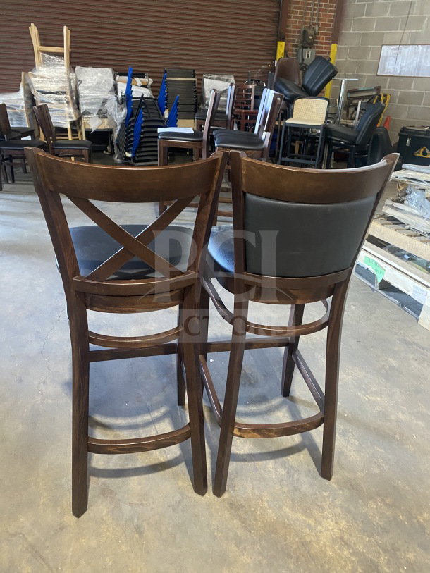 Brand new commercial mahogany wood bar stools with cushion back and black vinyl seat, shown in warehouse.