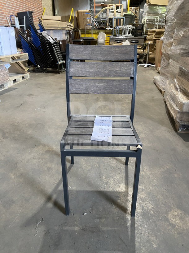 Brand new commercial outdoor teak chair with gray slats, black metal frame. Perfect condition. Auction tag visible on seat.