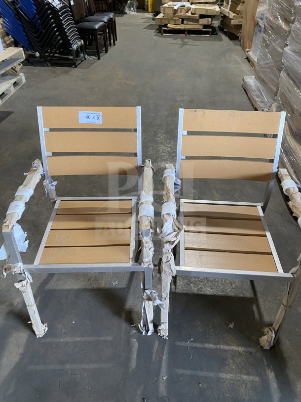 Brand new aluminum outdoor arm chairs with tan synthetic teak slats, stackable, auction label "40 x 2," wrapped for protection.