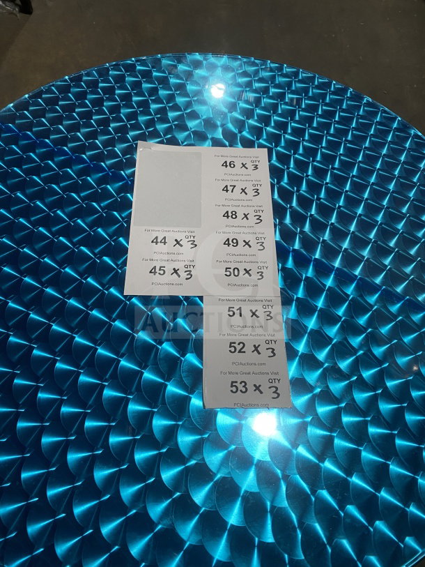 Brand new commercial stainless steel cocktail table with polished base, model D36. Features a metallic blue geometric pattern. Auction tags visible.