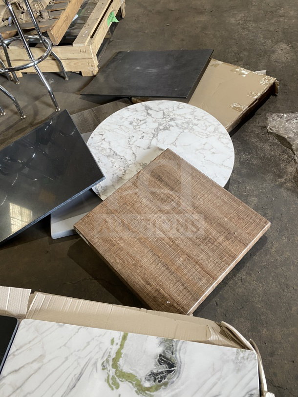 Assorted new commercial restaurant table tops in various shapes and finishes, displayed on the floor.
