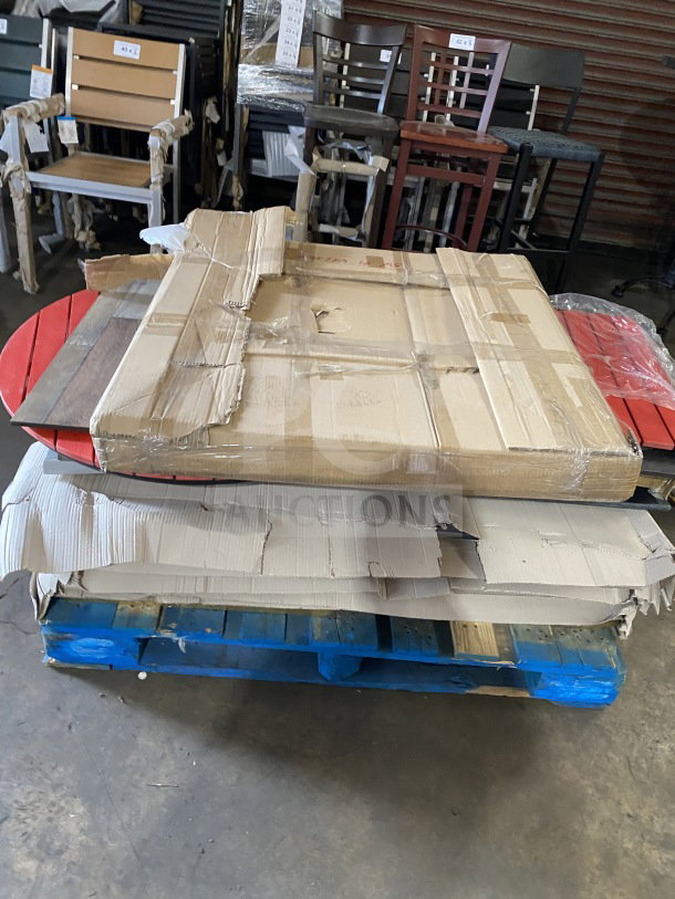 Brand new commercial restaurant and cafe table tops stacked on a pallet, partially wrapped in cardboard, ready for auction.