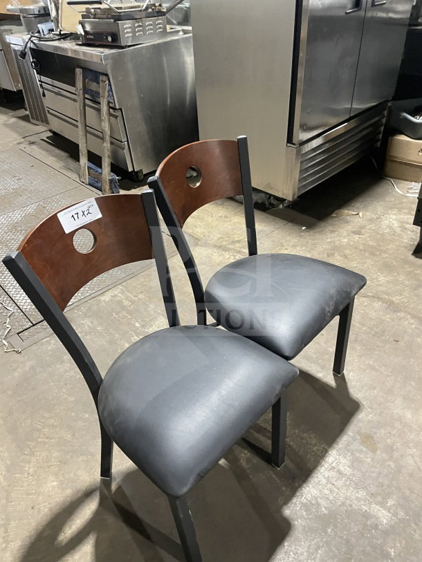 Brand new commercial dining chairs with cherry wood circle cutout backs, black vinyl seats, and sturdy metal frames.