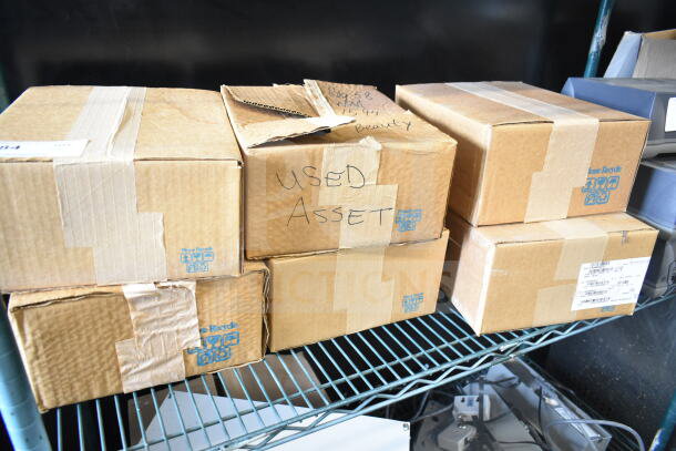 Cardboard boxes containing six used Sensormatic items, including ZBAMB9010-IPS, labeled as "Used Asset."