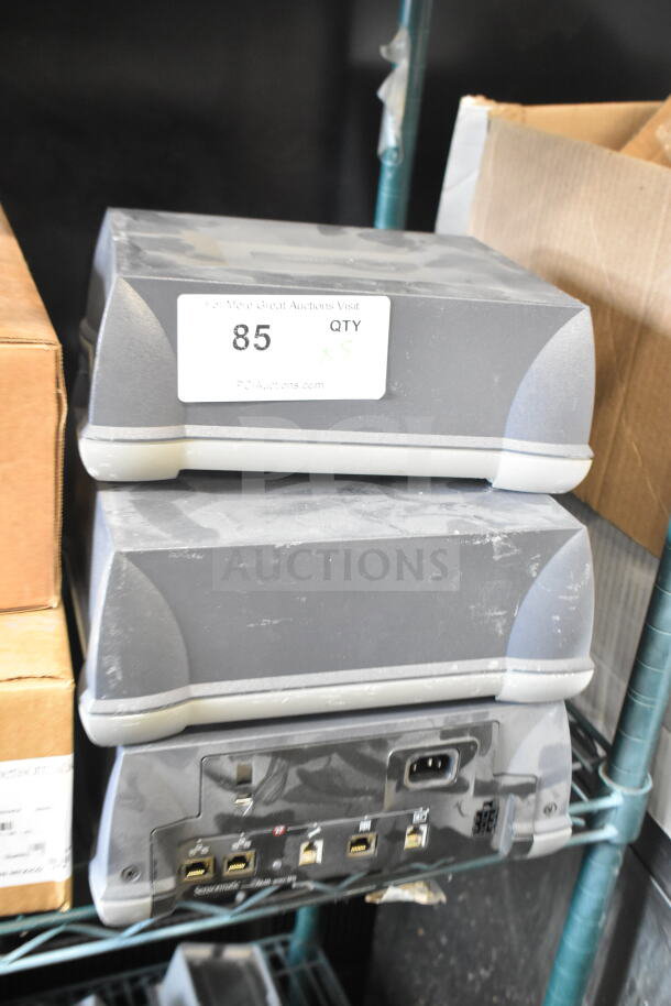 5 Sensormatic AMB-9010-IPS label deactivators, gray, stack on shelf. Dust present, port connections visible. Lot of 5.