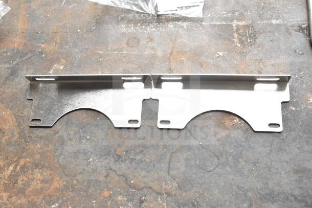 Two brand new metal burner brackets, scratch and dent condition, mounted on a worn surface.