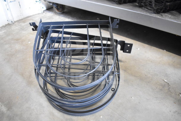 Lot of various metal racks stacked on a concrete floor, showing U-shaped wire design, in used condition.