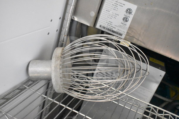 Three kitchen attachments, including a Pelican head, S blade for Pelican head, and a whisk attachment on a metal shelf.