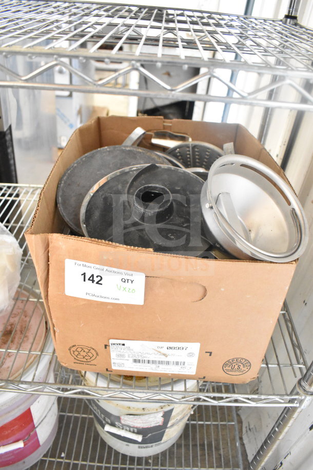 Cardboard box with various food processor blades. Box labeled "142 QTY Vx20" on a wire shelf, showing some metal and plastic blades.
