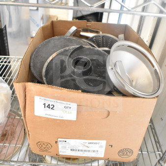 Cardboard box with various food processor blades. Box labeled "142 QTY Vx20" on a wire shelf, showing some metal and plastic blades.