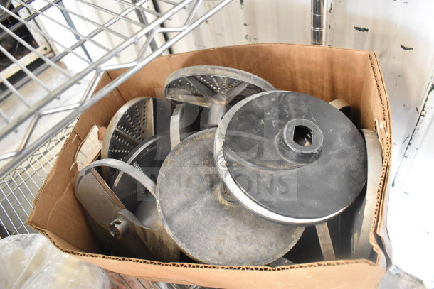 Cardboard box containing various food processor blades in used condition.