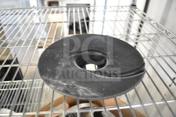 Black food processor blade disk on wire shelf, part of a lot of 20 various items. Some wear visible.