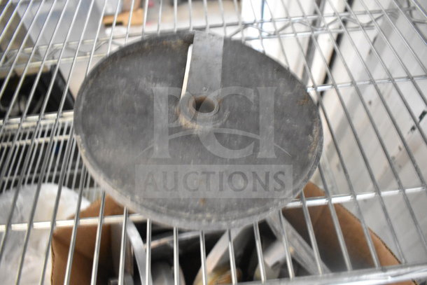 A collection of food processor blades and other items in a cardboard box on a metal shelf, showing wear.