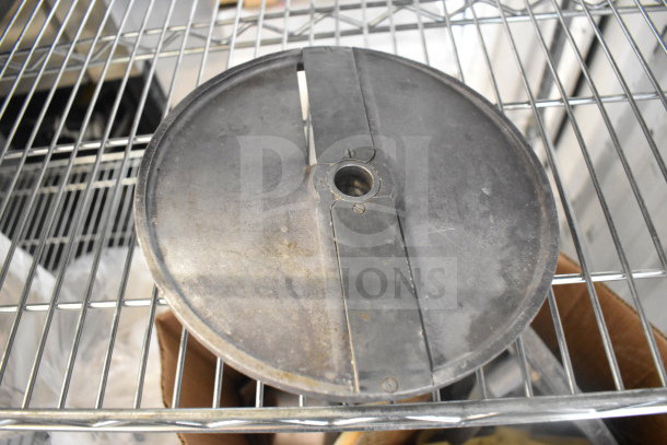 A large, circular metal food processor blade with a central hole, showing signs of use, on a metal shelf.