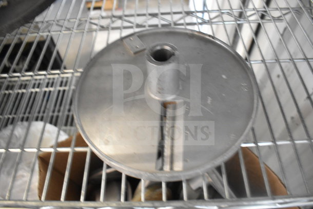 Metal food processor blade on a wire shelf, part of a lot of 20 various items. Blade appears used; no visible brand markings.