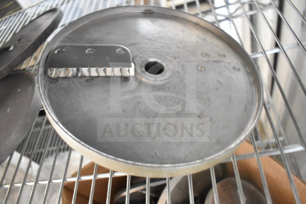 Metal food processor blade with serrated edge, part of a set of 20 items. Visible on metal rack, in used condition.
