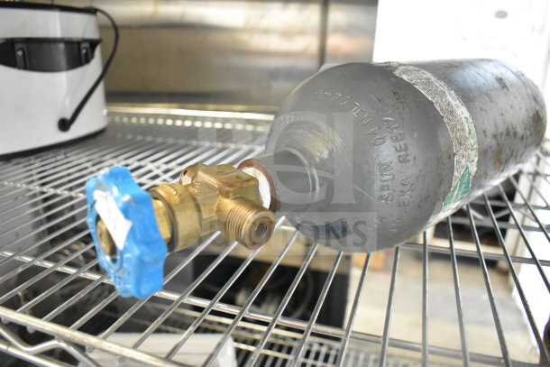 Carbon dioxide tank, gray metal with blue valve, visible markings, moderate wear, placed on metal shelf. Buyer pick-up only.
