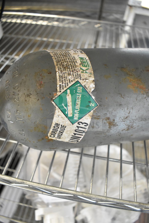 Carbon dioxide tank with worn "Non-Flammable Gas" label, UN1013 marking, visible rust, and text indicating buyer pick-up required.