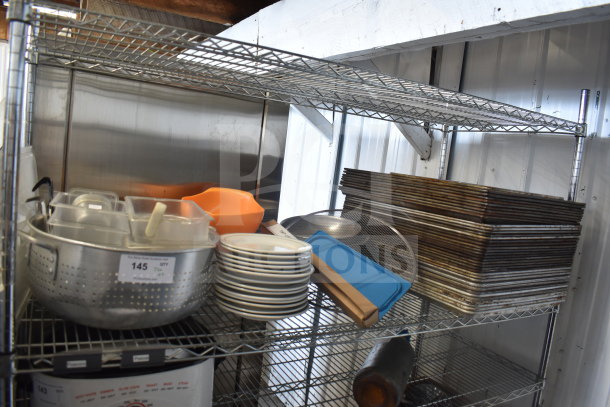 Tiered lot including metal colander, stack of plates, baking pans. Visible tag: "145 QTY." Various kitchen essentials.