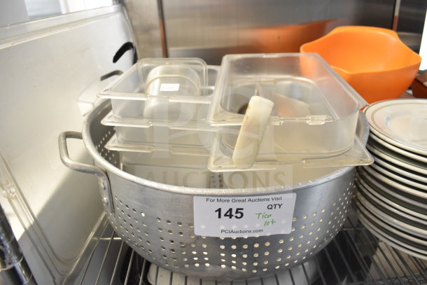 A collection of kitchen items including a metal colander with perforations, stacked plastic containers, and a set of white plates.