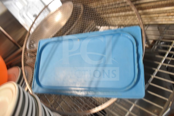 Tiered lot with a metal colander, blue baking tray, and assorted plates on wire shelving. Items in used condition.