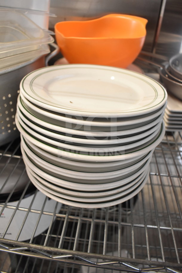 Stack of white plates with green rims on a wire shelf, alongside an orange plastic bowl and metal colander. Auction lot.