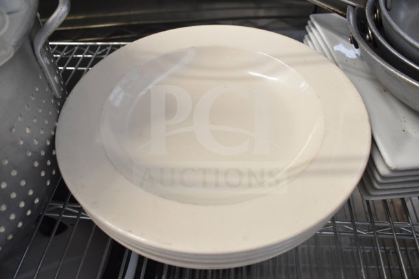 Tiered auction lot featuring a white plate, metal colander, and stacked baking pans on a shelf. Items in used condition.