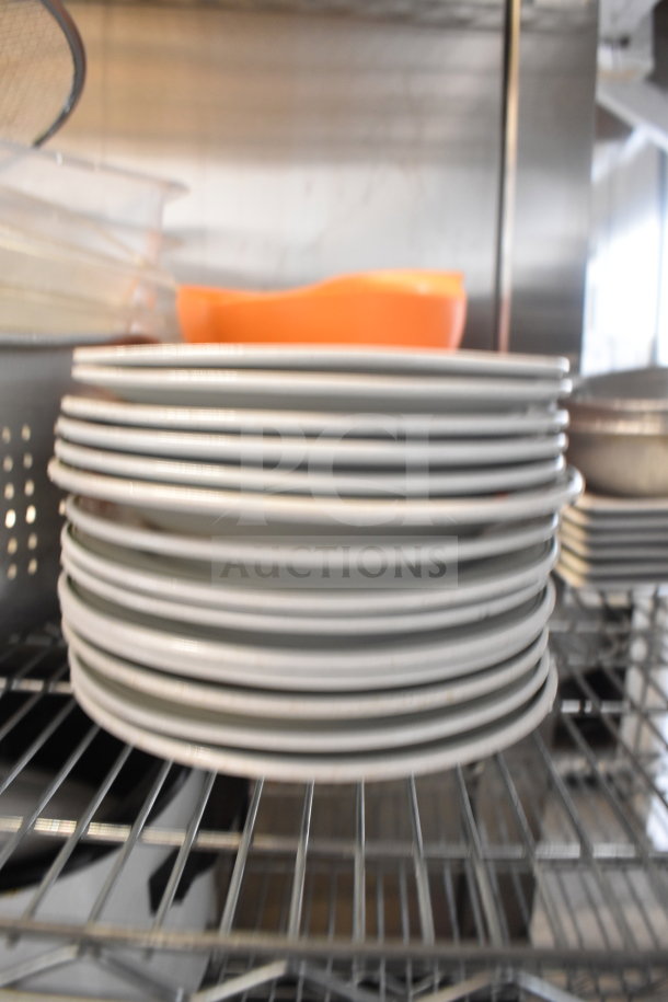 Stack of white plates, metal colander, orange bowl, and baking pans on a metal shelf. Items in used condition.