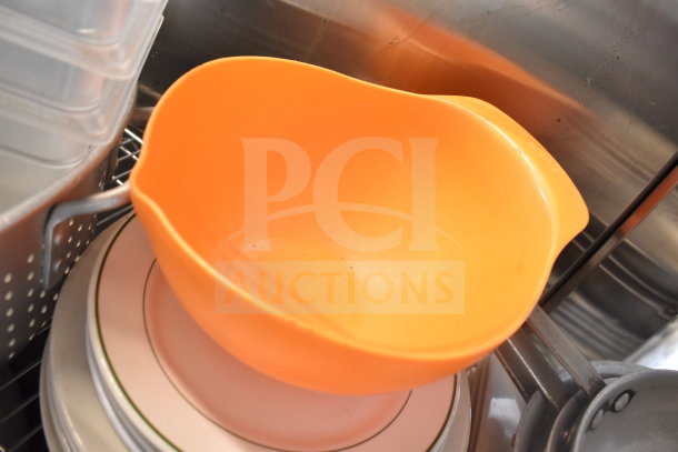 Orange plastic colander, stack of plates, and various baking pans in tiered lot auction. Good condition kitchenware.
