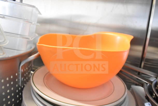 Assorted kitchenware lot with orange colander, stack of plates, and baking pans; gently used condition.
