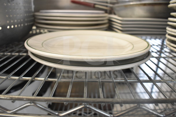 Stacked plates on metal shelf, beside a perforated colander and baking pans. Industrial kitchen setting.