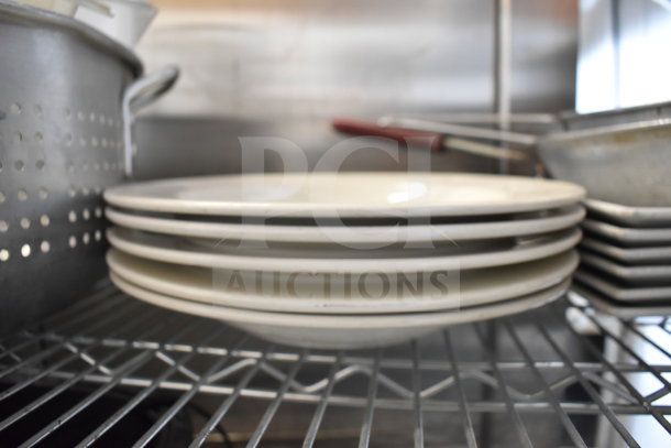 Stack of white plates with metal colander and baking pans on wire shelf; part of tier lot auction.