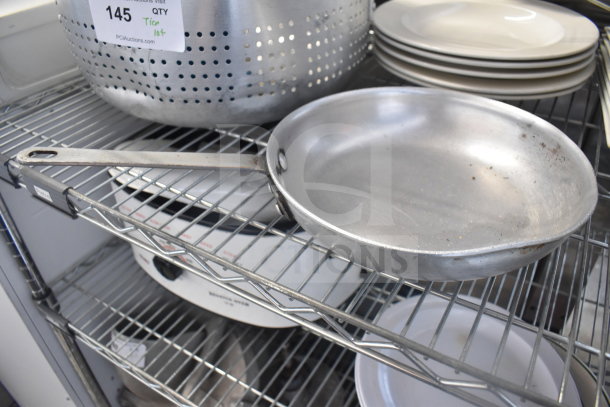 Tiered lot of kitchen items including a metal colander, stack of white plates, and a metal baking pan. Visible tag indicates lot 145.