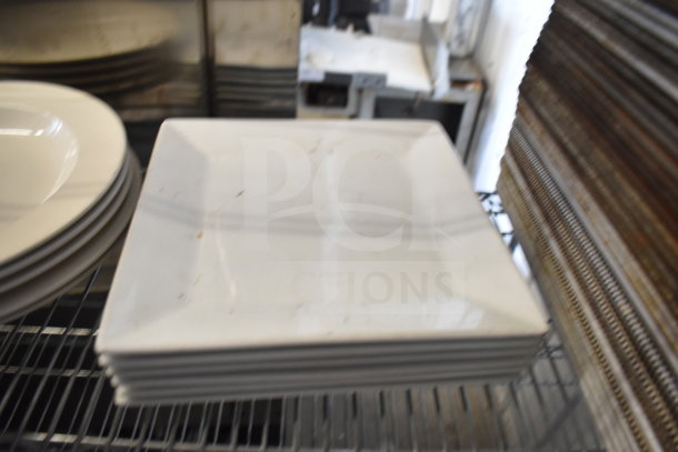 Stacked white square plates on metal rack, part of an auction lot including colander and baking pans. Plates appear gently used.