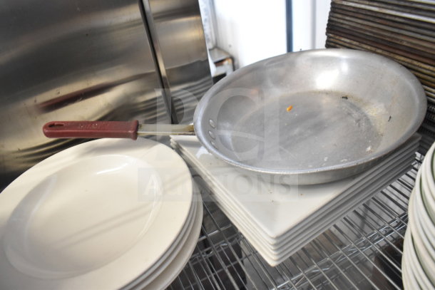 Auction lot with metal colander, white plates, and baking pans. Mixed condition, ideal for kitchen basics.