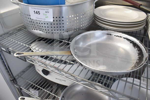 Tiered lot with metal colander, stack of white plates, and baking pans on a metal rack. Auction label QTY 145.